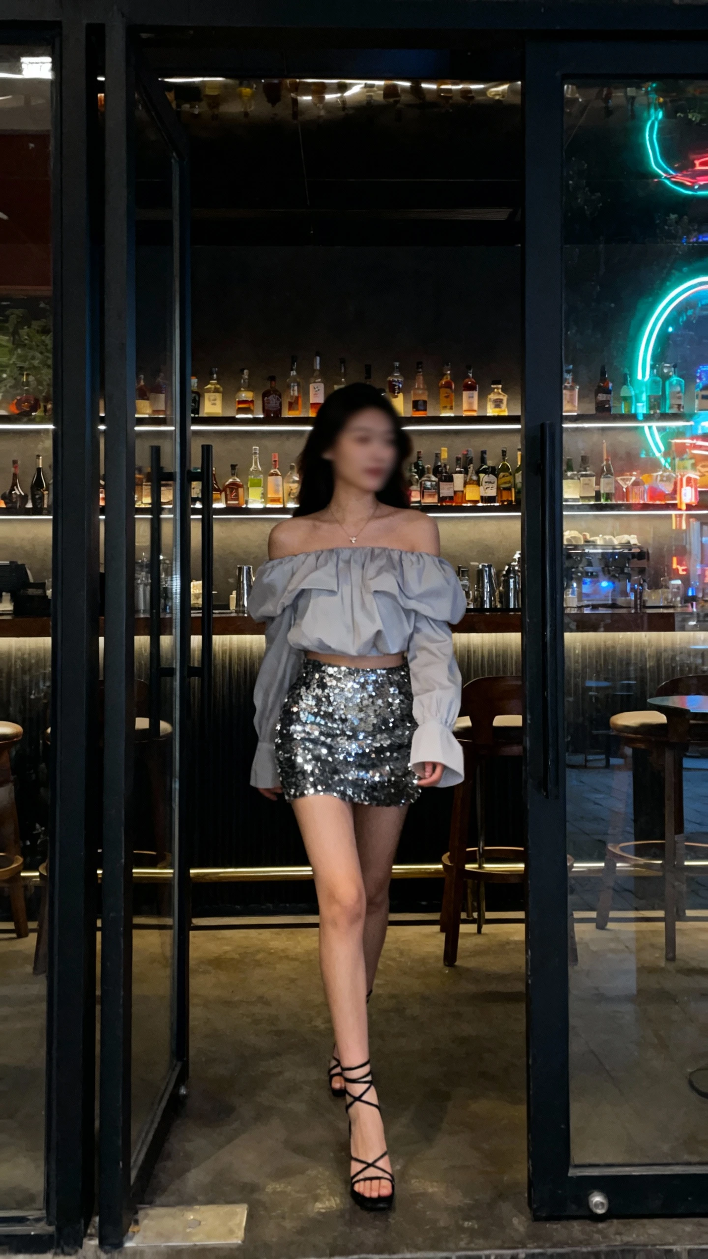 Natural nightlife photo of a woman in a statement shoulder top and a sequin mini skirt with strappy heels, walking into a dimly lit cocktail bar, face slightly blurred, neon reflections, iPhone photo quality.
