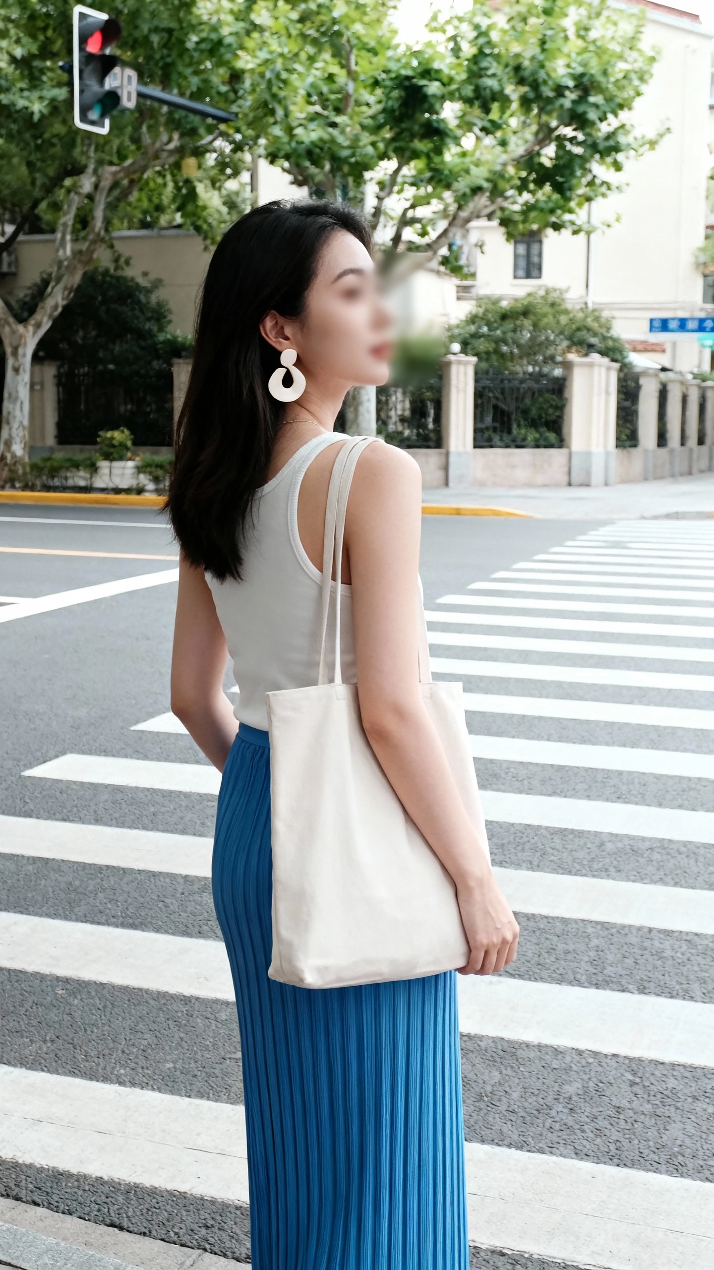 Candid photo of a woman wearing a blue column skirt and a simple tank with sculptural earrings and a minimalist tote, waiting at a crosswalk, face slightly blurred, soft daylight, iPhone photo quality.