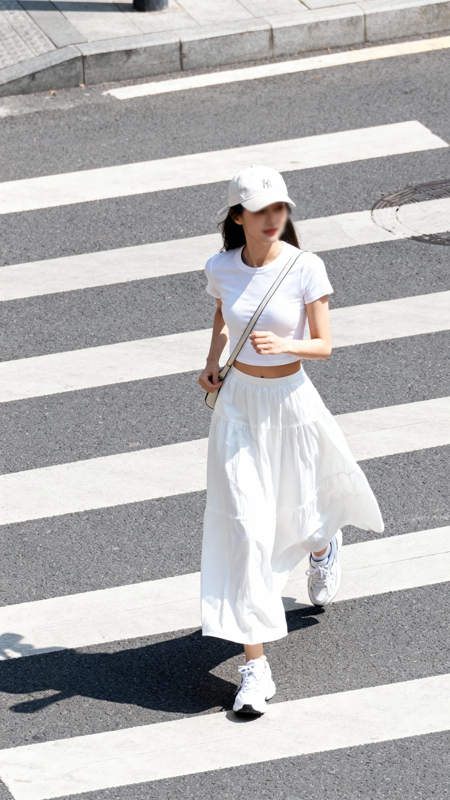 Candid photo of a woman wearing a white maxi skirt with a fitted cropped tee and clean white sneakers, baseball cap and crossbody bag, power-walking across a city crosswalk, face slightly blurred, bright daylight, casual iPhone aesthetic.
