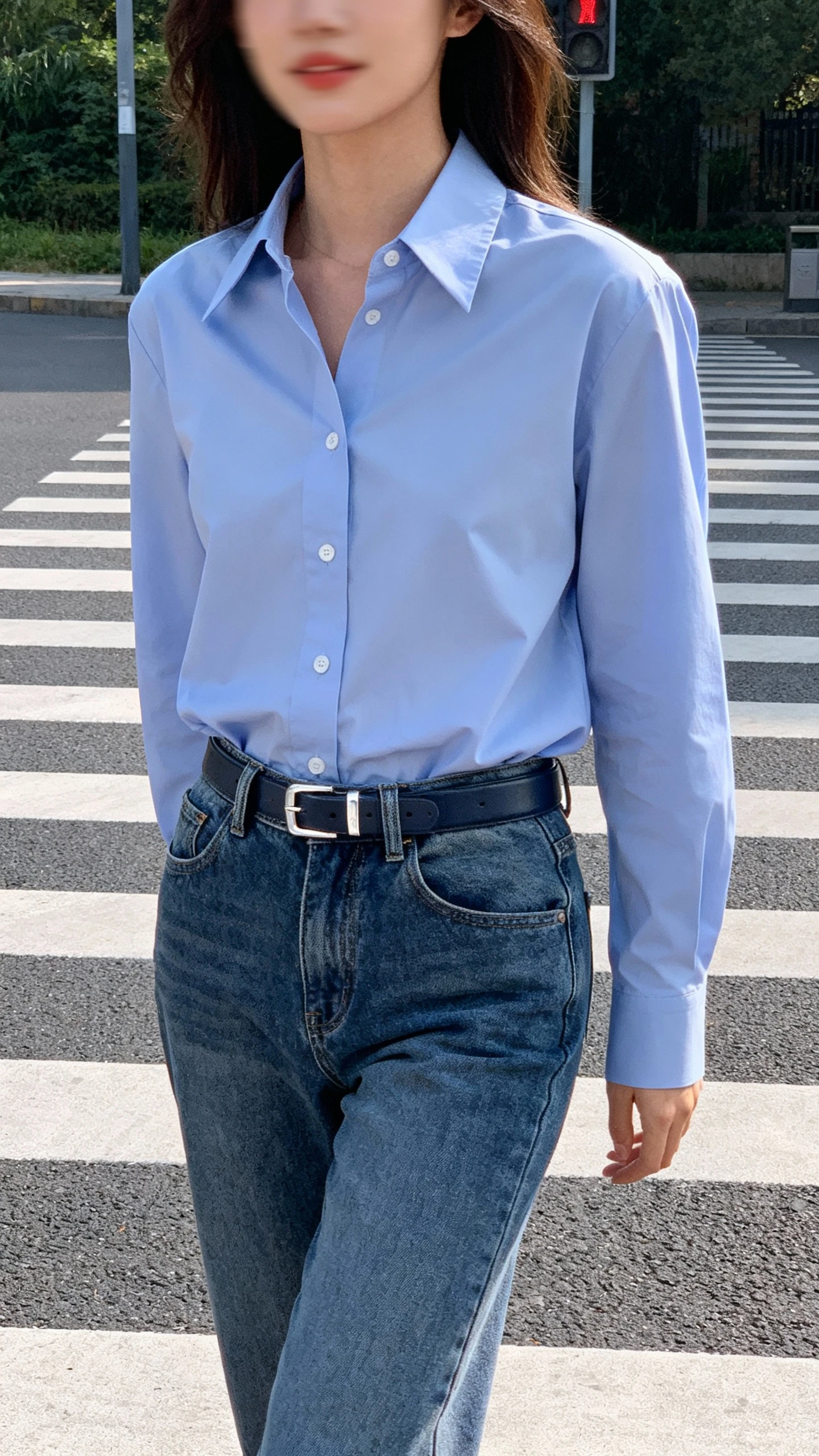 Candid photo of a woman wearing low-rise jeans with a crisp button-down shirt tucked in and a sleek belt, standing at a crosswalk, face slightly blurred, polished yet casual, afternoon daylight, iPhone photo quality.