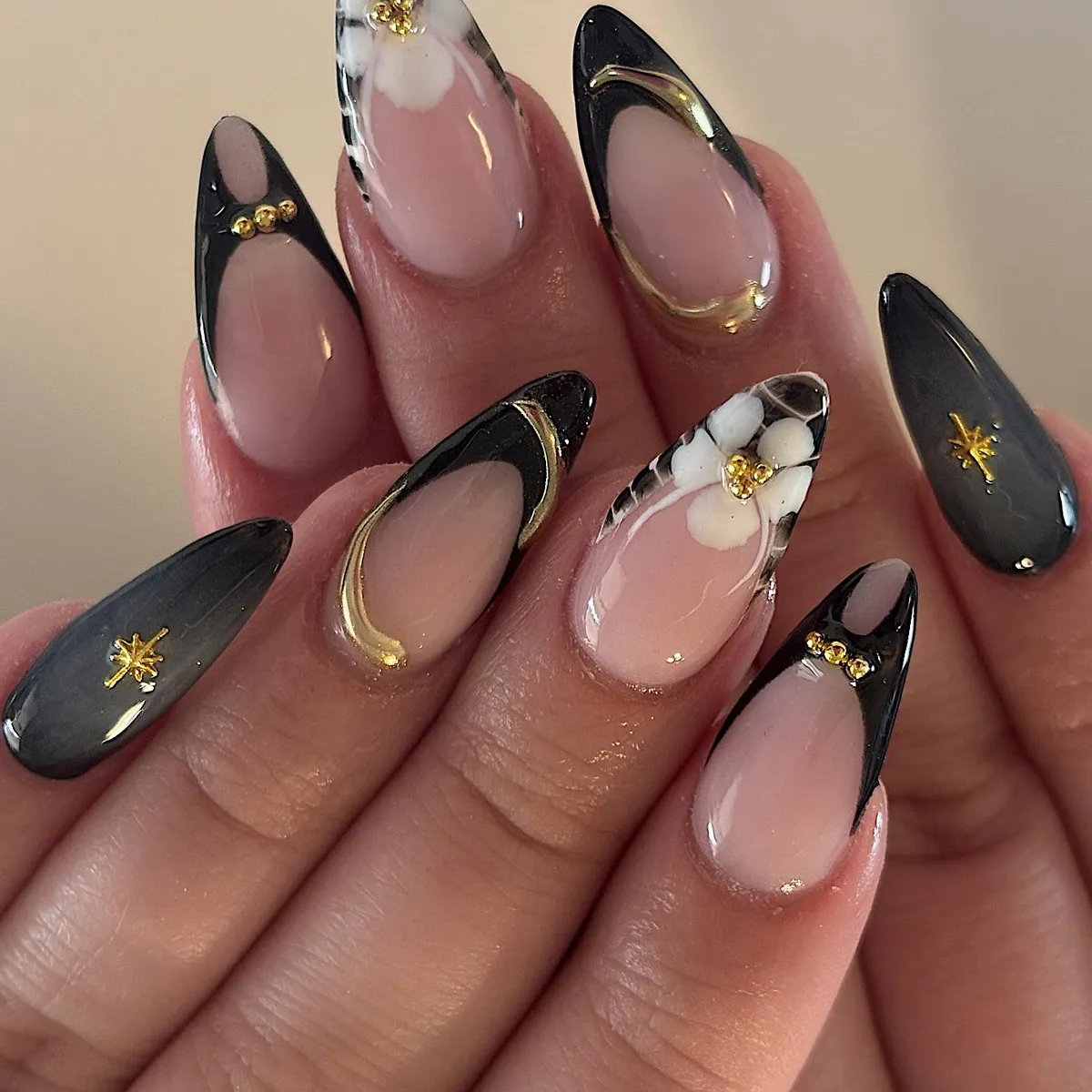 Black-framed nude nails with gold outlines and floral accent