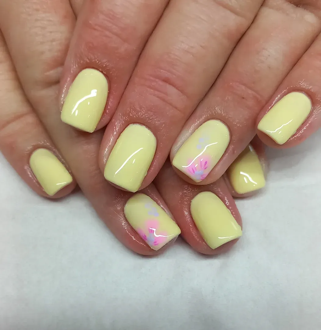 Pale yellow glossy nails with small pink-and-lilac corner accents