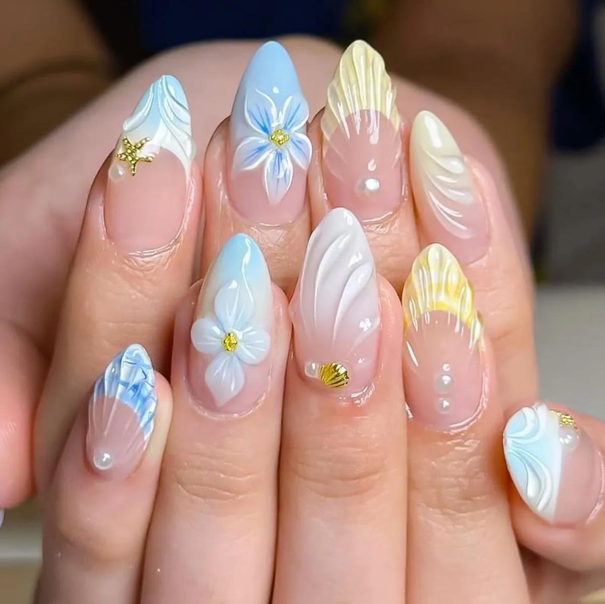 Sheer nude nails with raised waves, 3D flowers, and gold charms