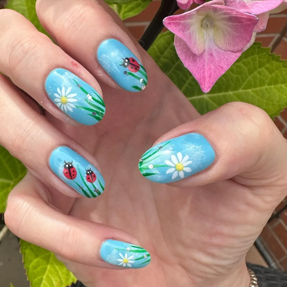 Sky-blue floral nails with ladybugs and grass details