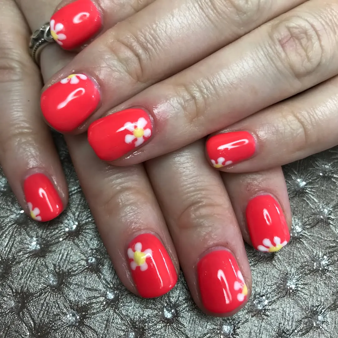 Coral-red nails with small white-and-yellow flowers
