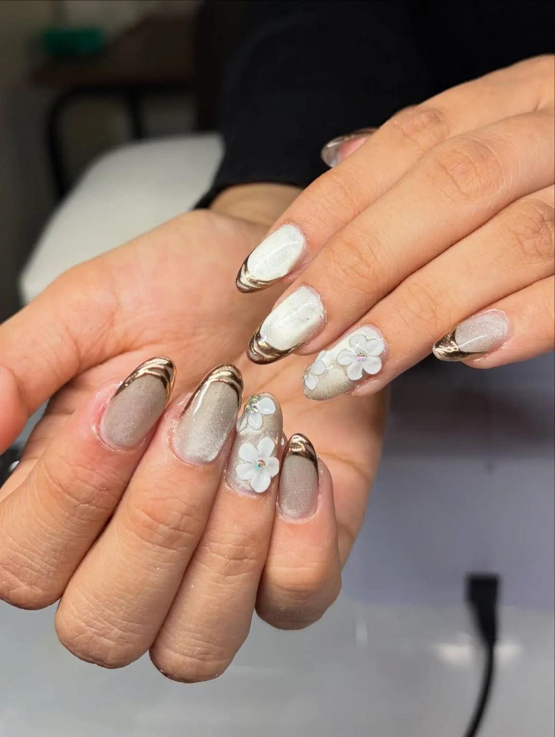 Shimmery neutral nails with metallic French tips and 3D white flowers