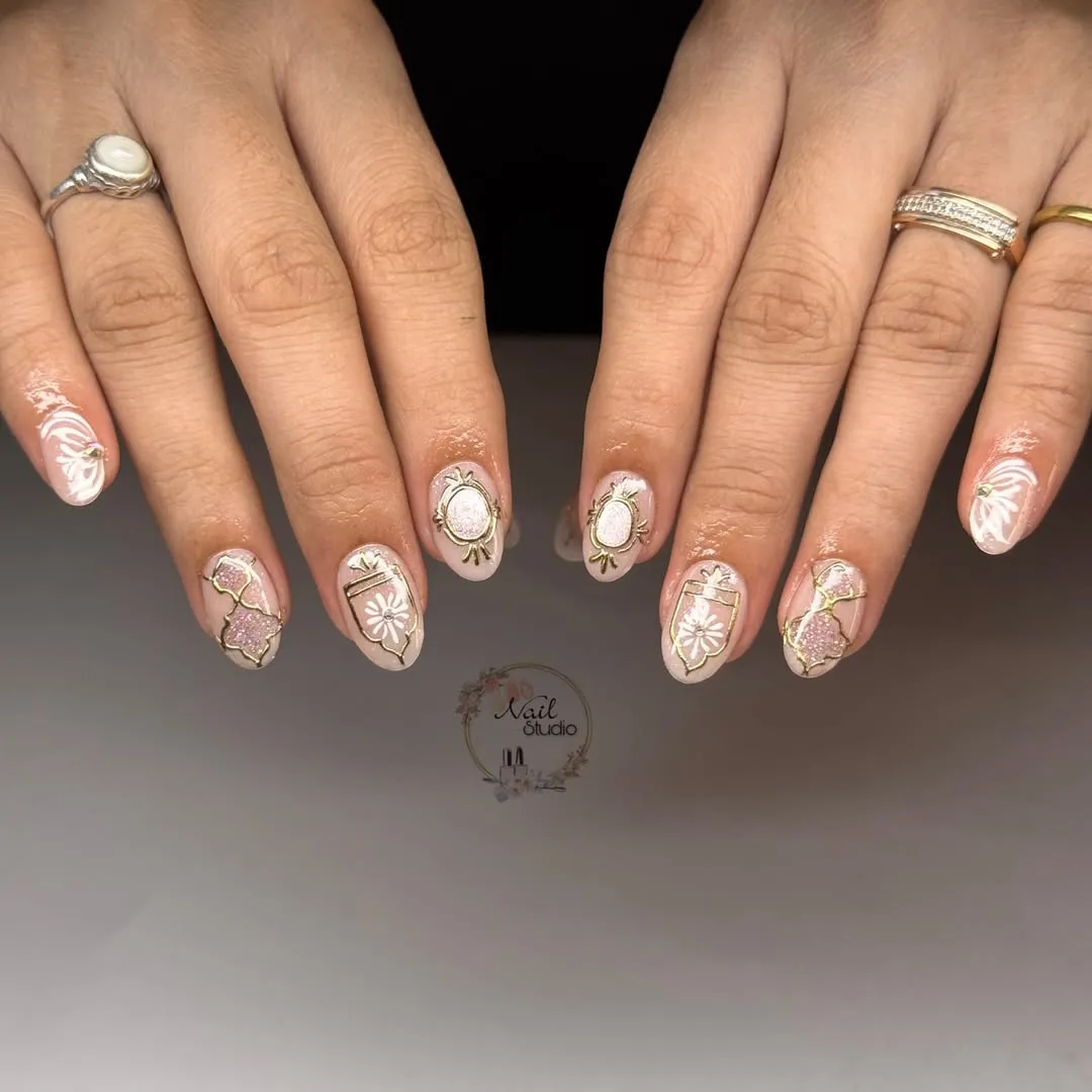 Pale pink almond nails with gold framing and white floral motifs