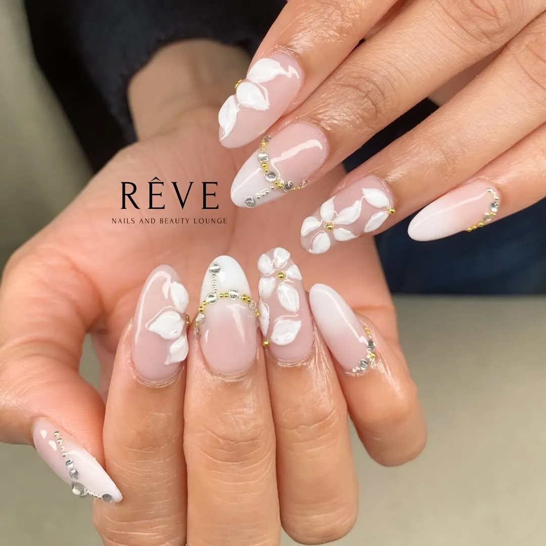 Long pale pink nails with raised white florals and bead/rhinestone curves
