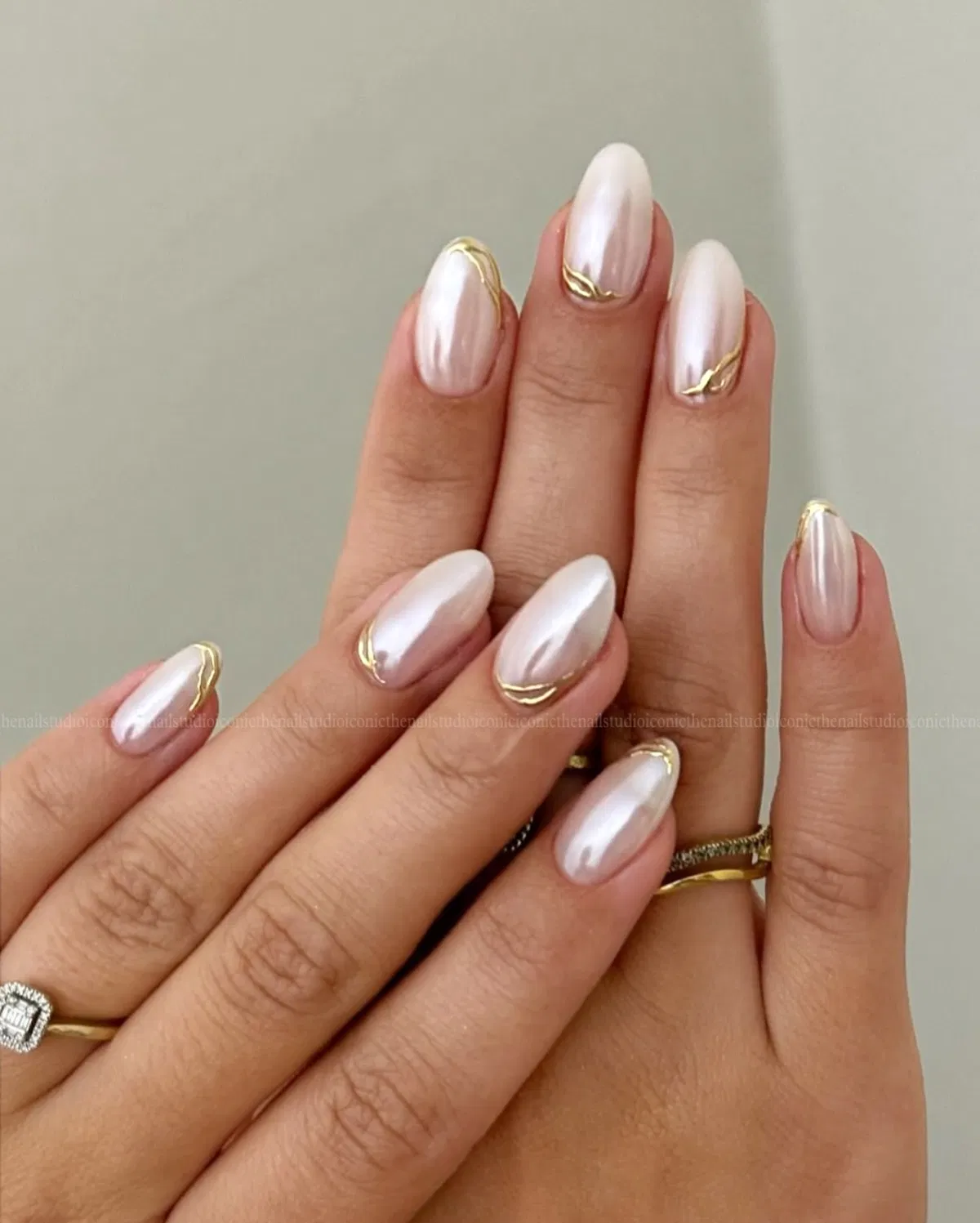 Pearly white almond nails with thin gold cuticle curves