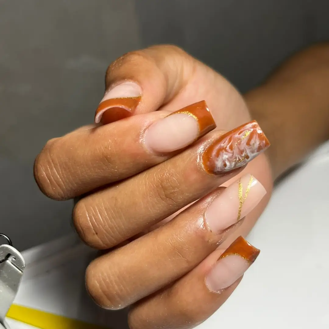 Burnt-orange French tips with swirled accent and gold lines