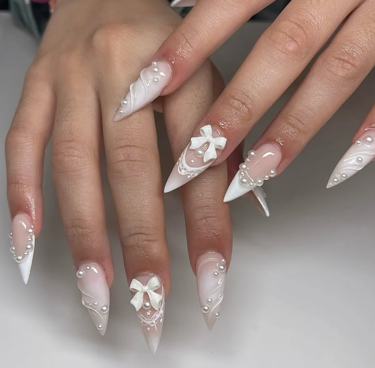 Pearl-embellished stiletto nails with raised bows and lace details