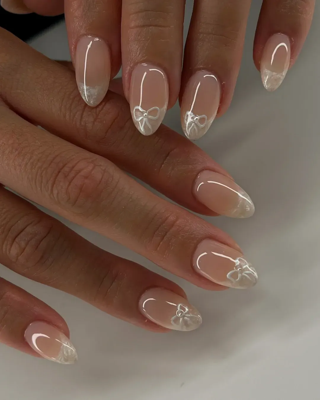 Nude almond nails with soft white tips and bow details