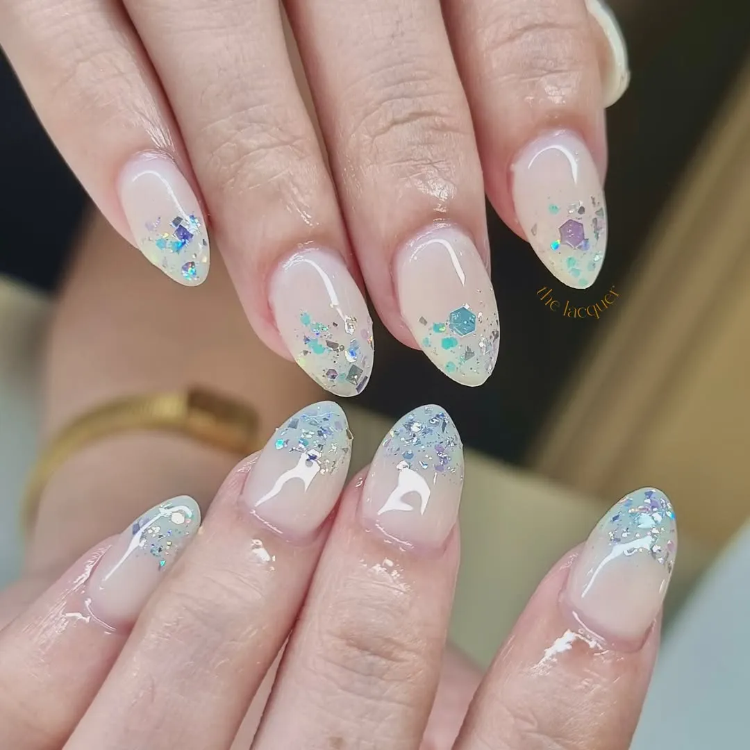 Sheer nude almond nails with iridescent confetti gradient tips