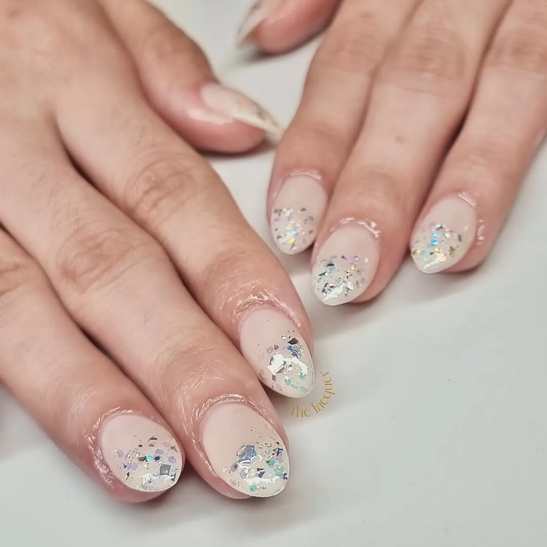 Sheer nude nails with iridescent confetti tips
