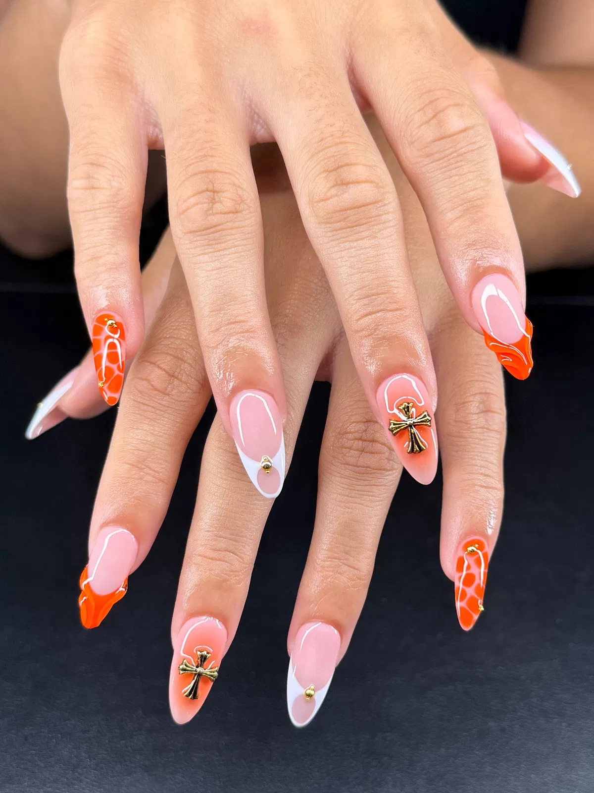 Pink-nude base with orange webbed tips, white French accents, and gold cross charms