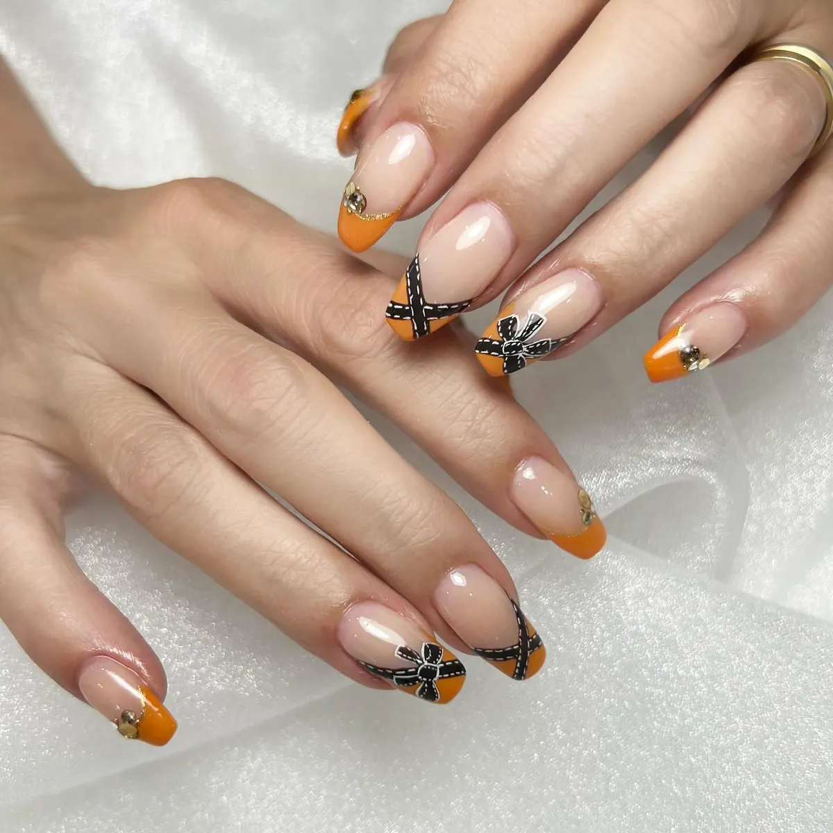 Nude nails with orange tips and black stitched-style accents