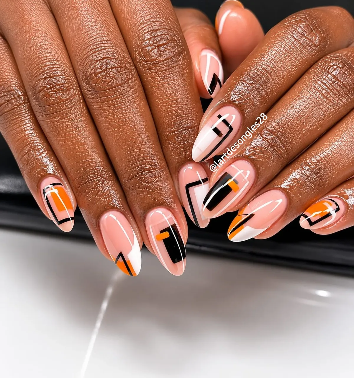 Nude-pink nails with black geometry and orange accents