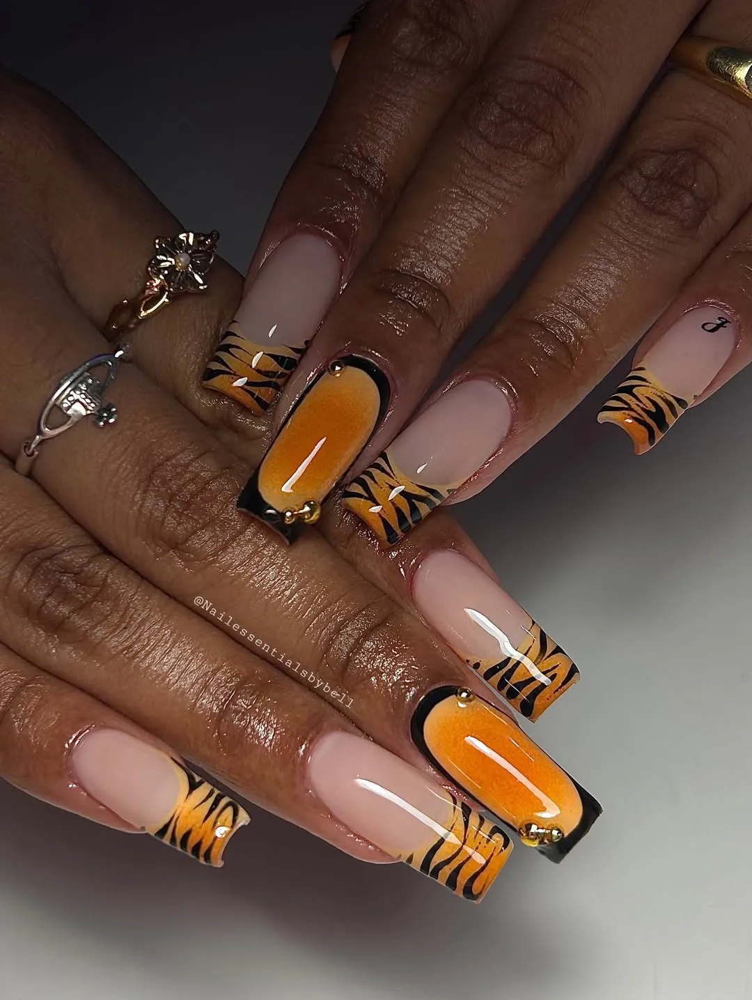 Nude-pink nails with orange/black striped tips and gradient panels