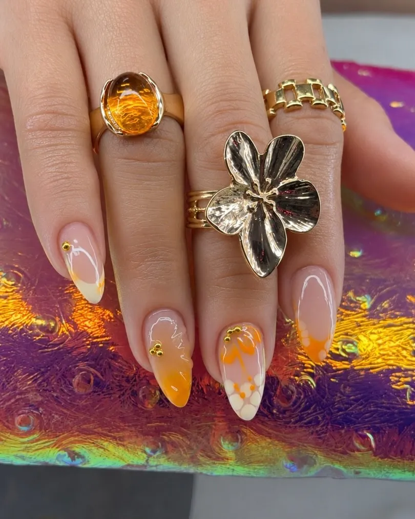 Nude almond nails with orange-and-white accents and gold studs