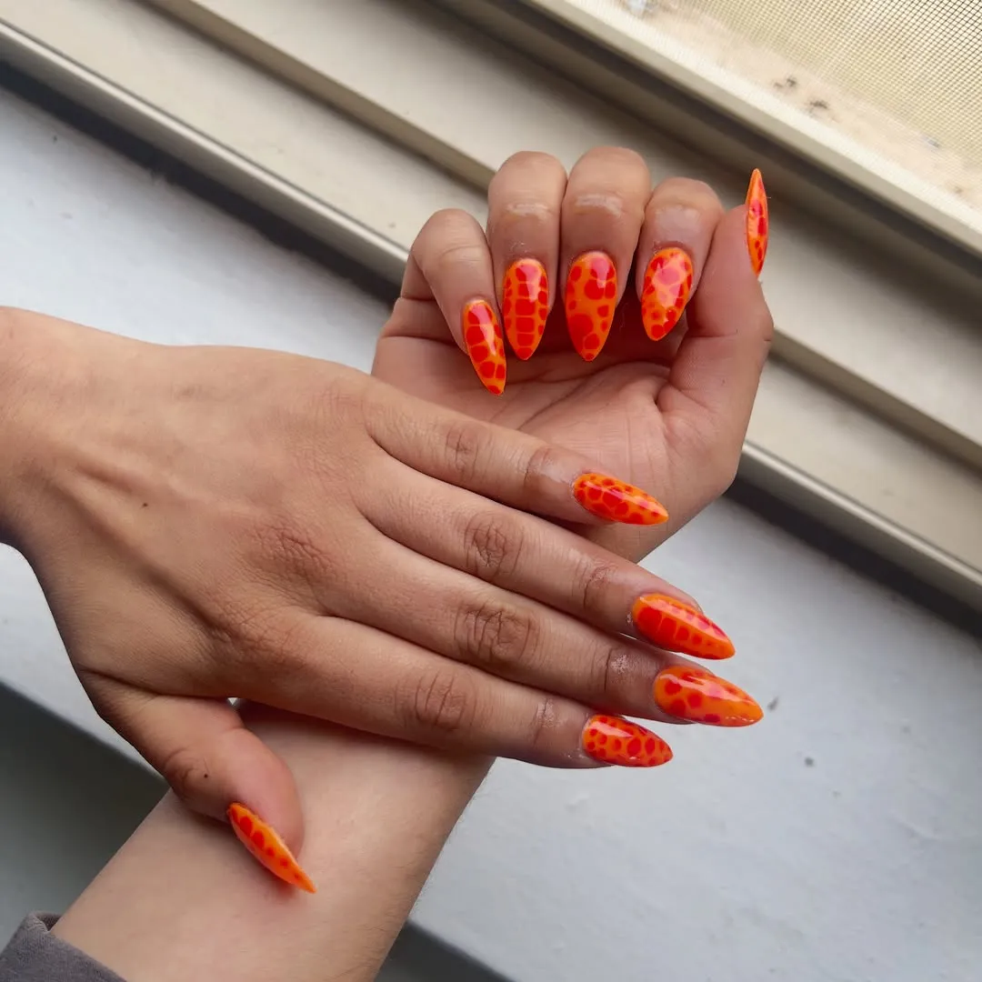 Orange stiletto nails with irregular spot pattern