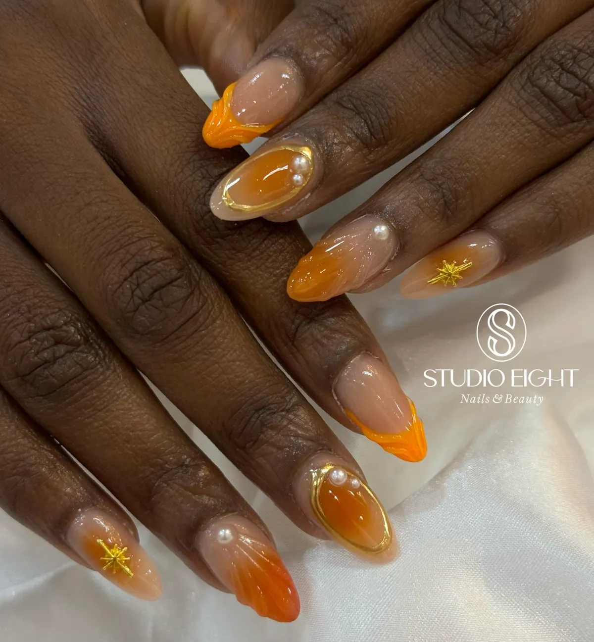 Orange ombrรฉ tips with gold-framed accents and pearls