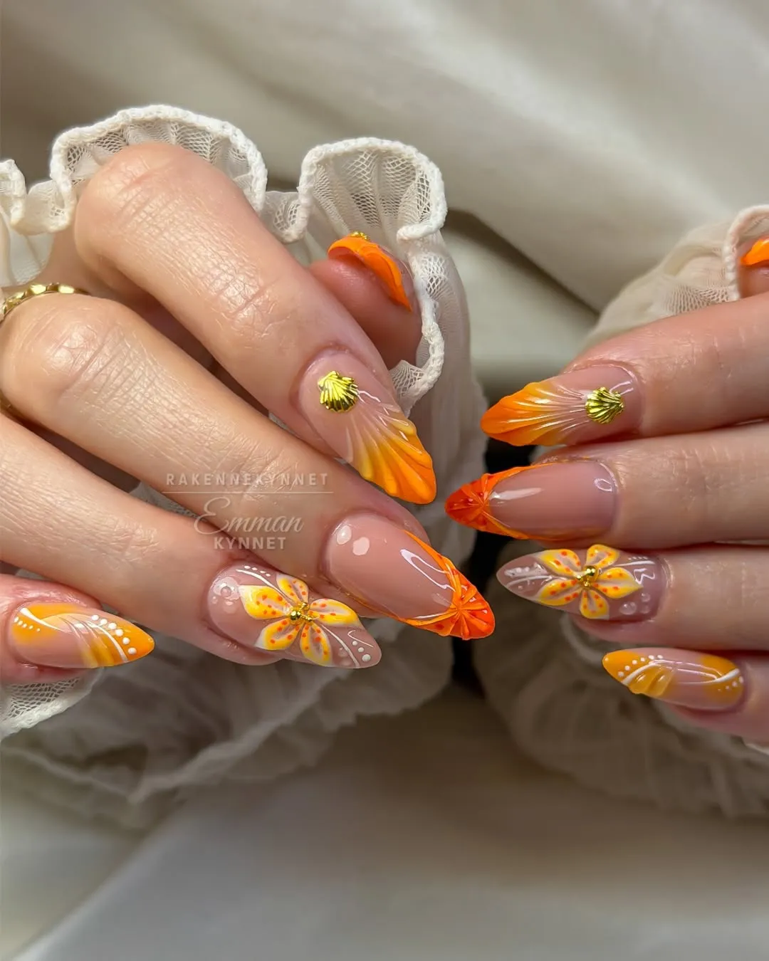 Orange gradient tips with 3D petals, gold shell charms, and floral accents