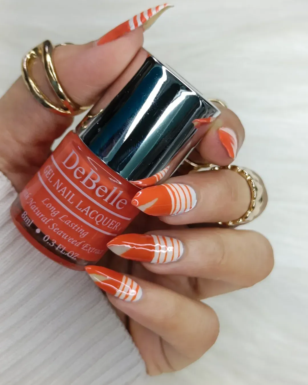 Orange-and-white curved stripes with visible nail lacquer bottle