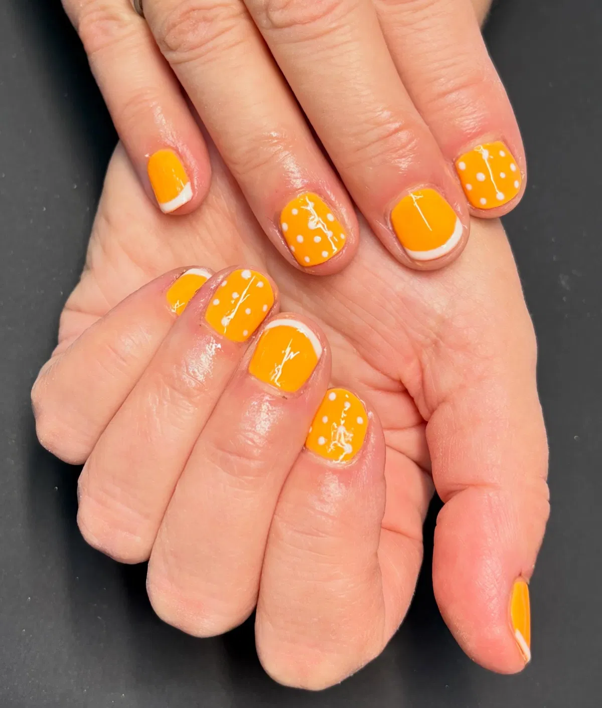 Short yellow-orange nails with polka dots and white curves