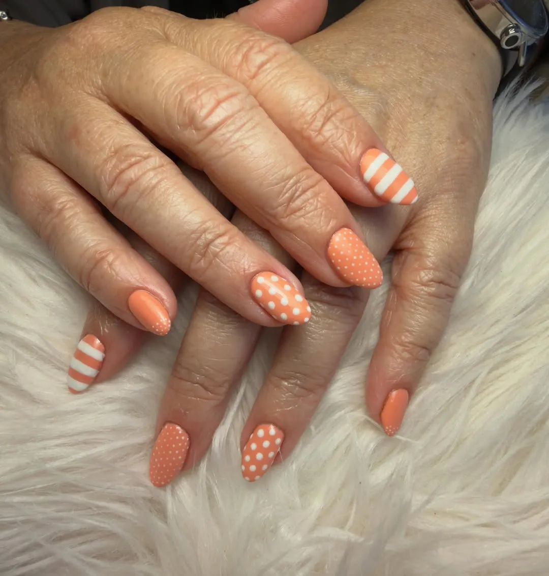 Peach-orange almond nails with white polka dots and stripes