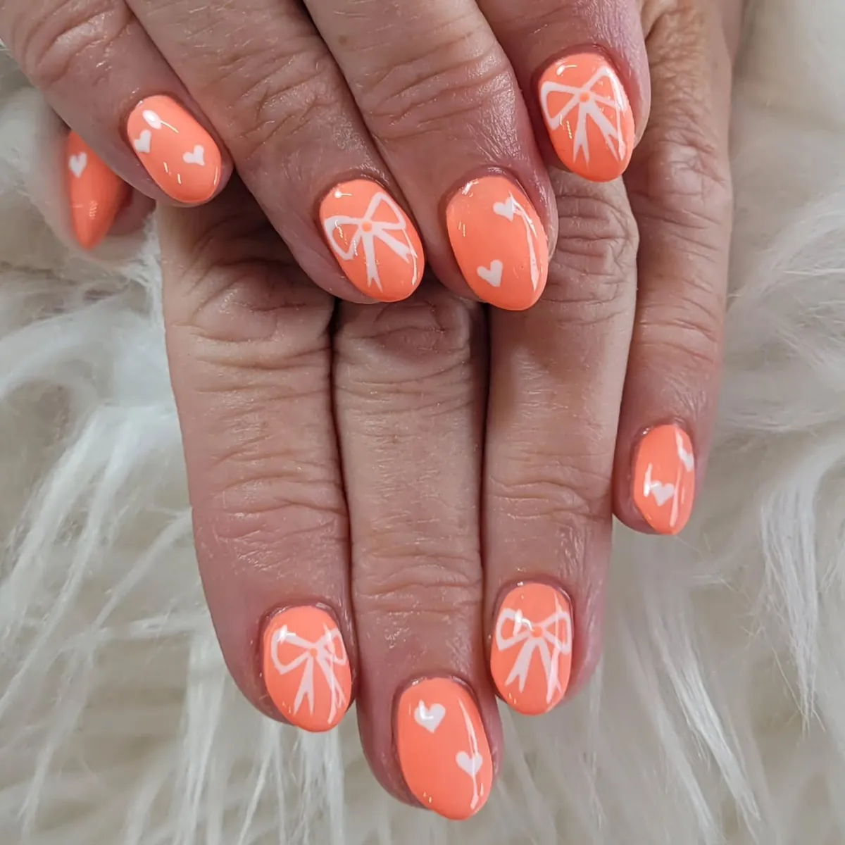 Pastel orange nails with white hearts and bows