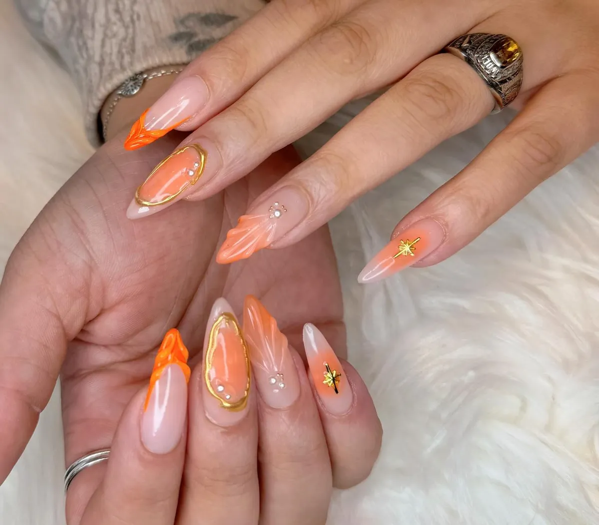 Almond nude nails with orange raised swirls, gold outlines, and rhinestones