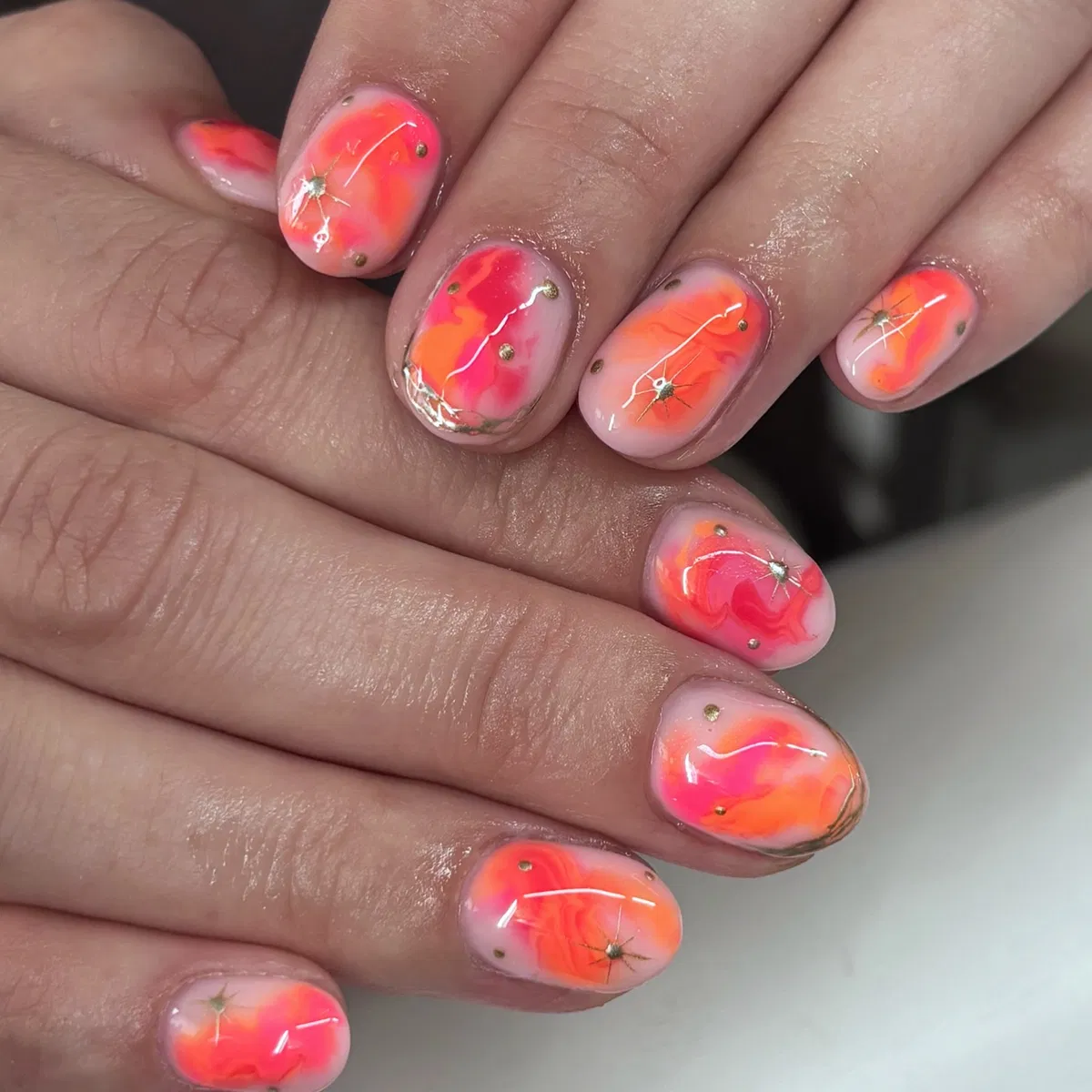 Short nude nails with pink-orange marbling and gold studs