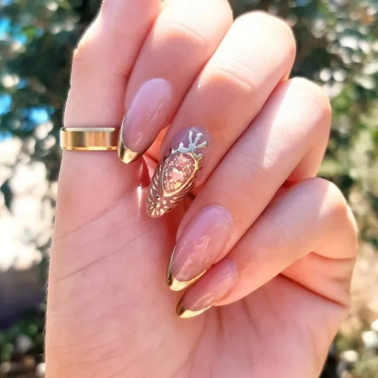 Nude almond nails with gold French tips and ornate framed accent