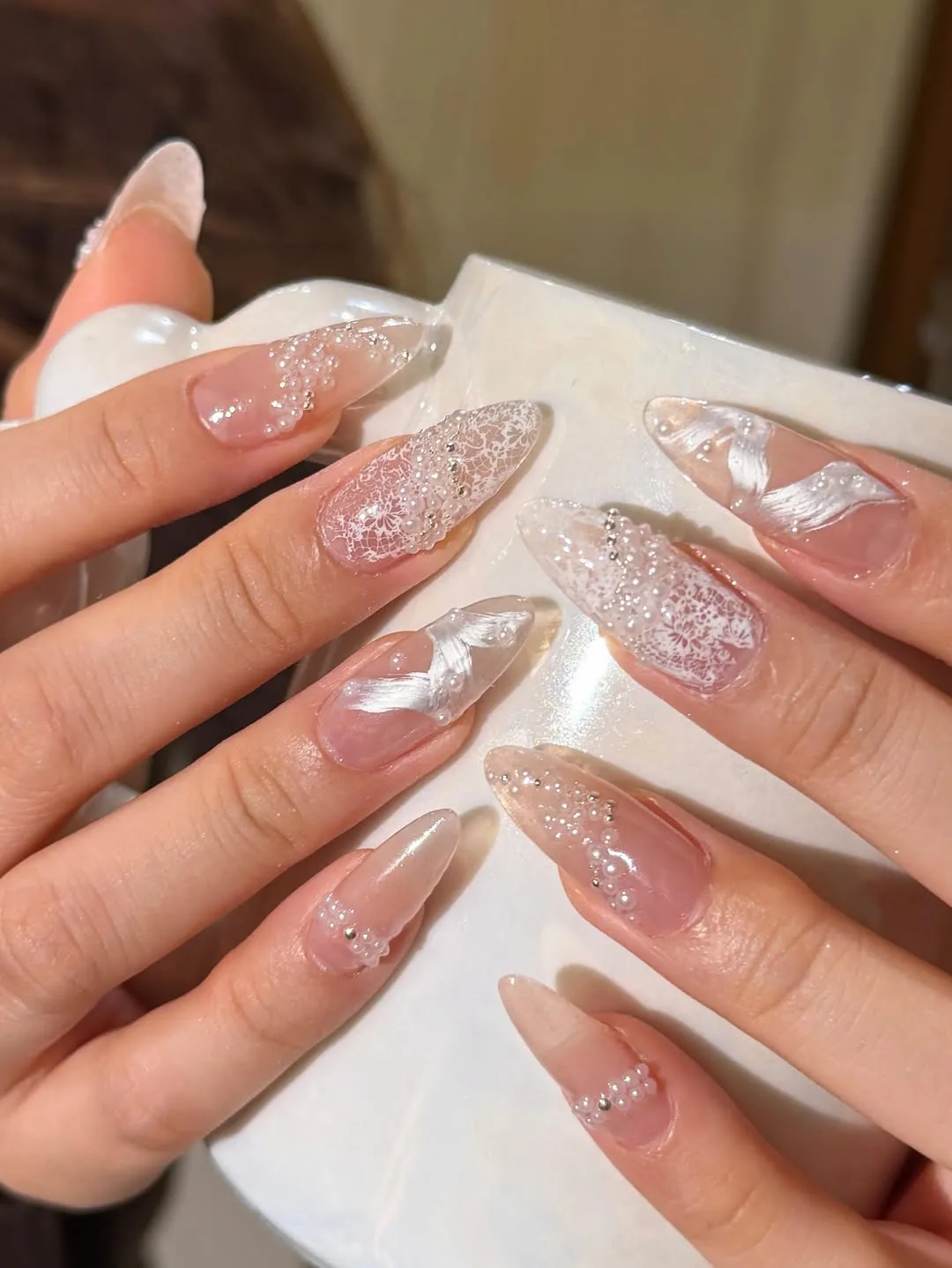 Glossy almond nails with lace print, bead clusters, and bow-like accents
