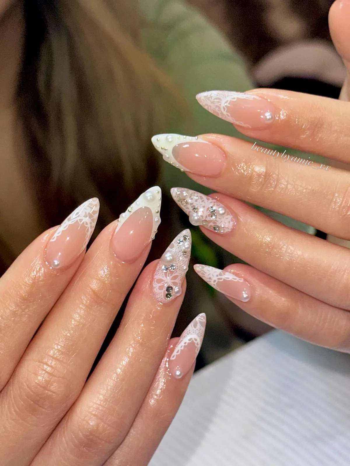Nude-pink stiletto nails with lace tips, pearls, and rhinestones