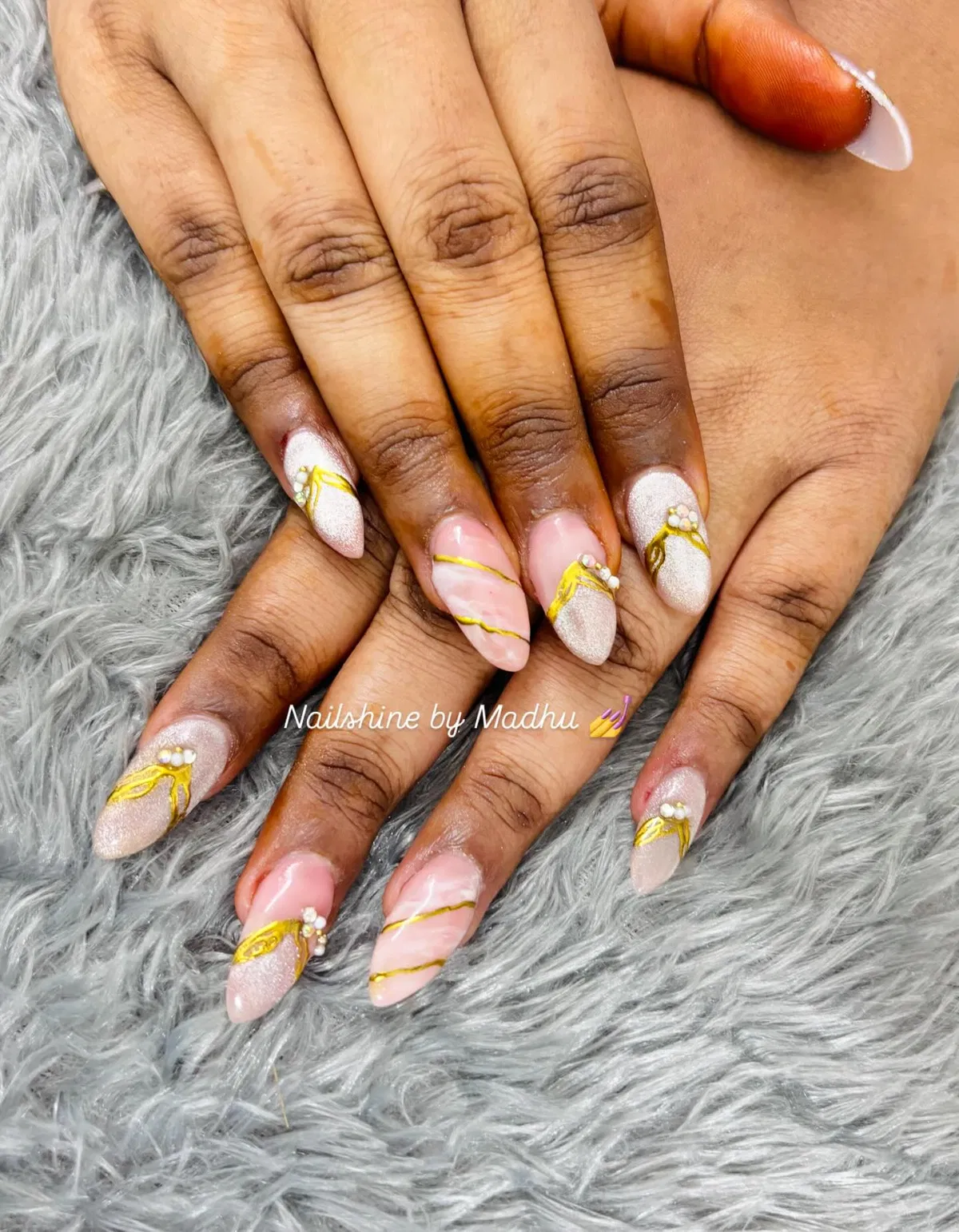 Pink and shimmery almond nails with gold waves and pearl clusters