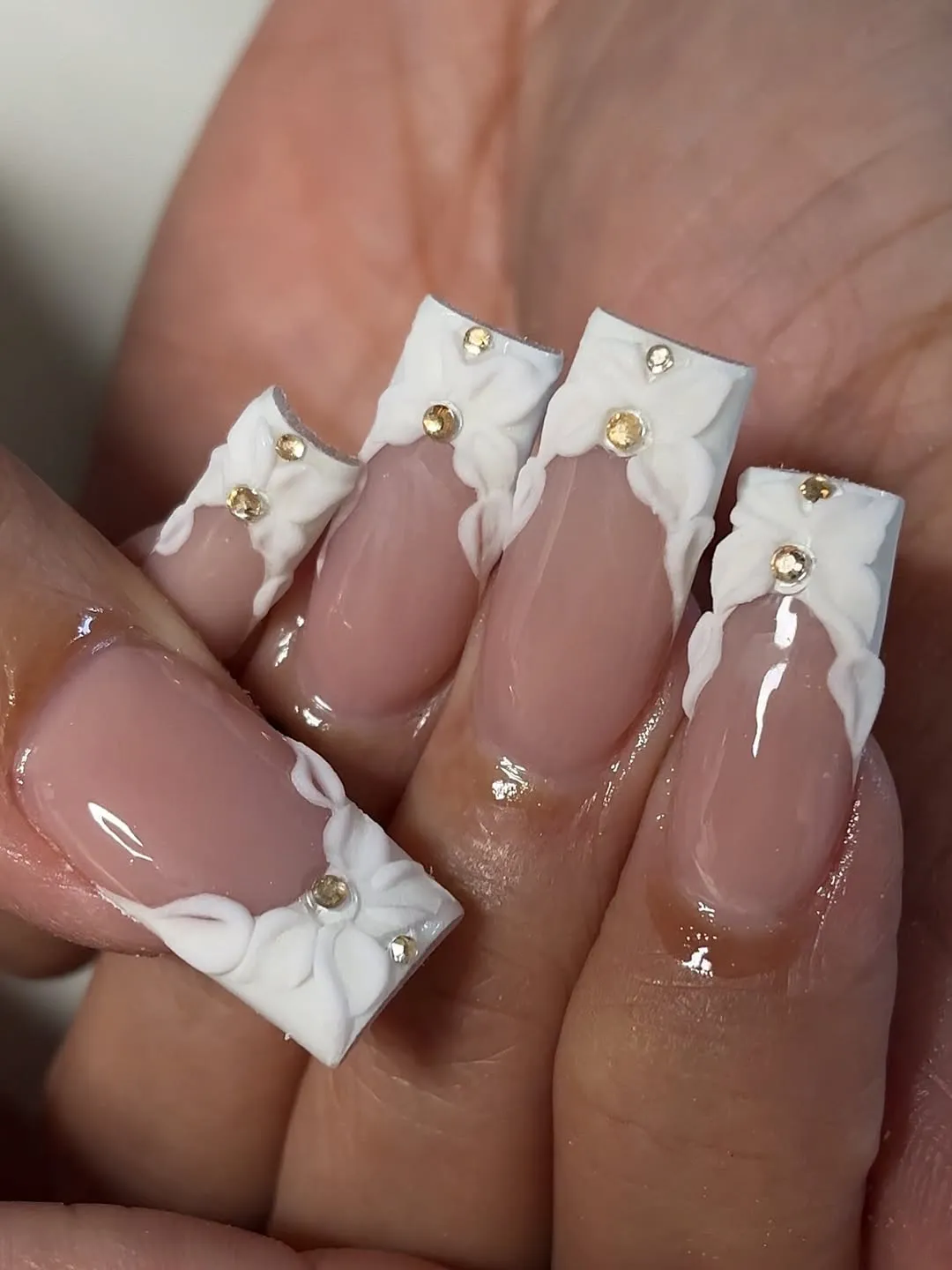 Nude square nails with raised white floral corners and gold studs