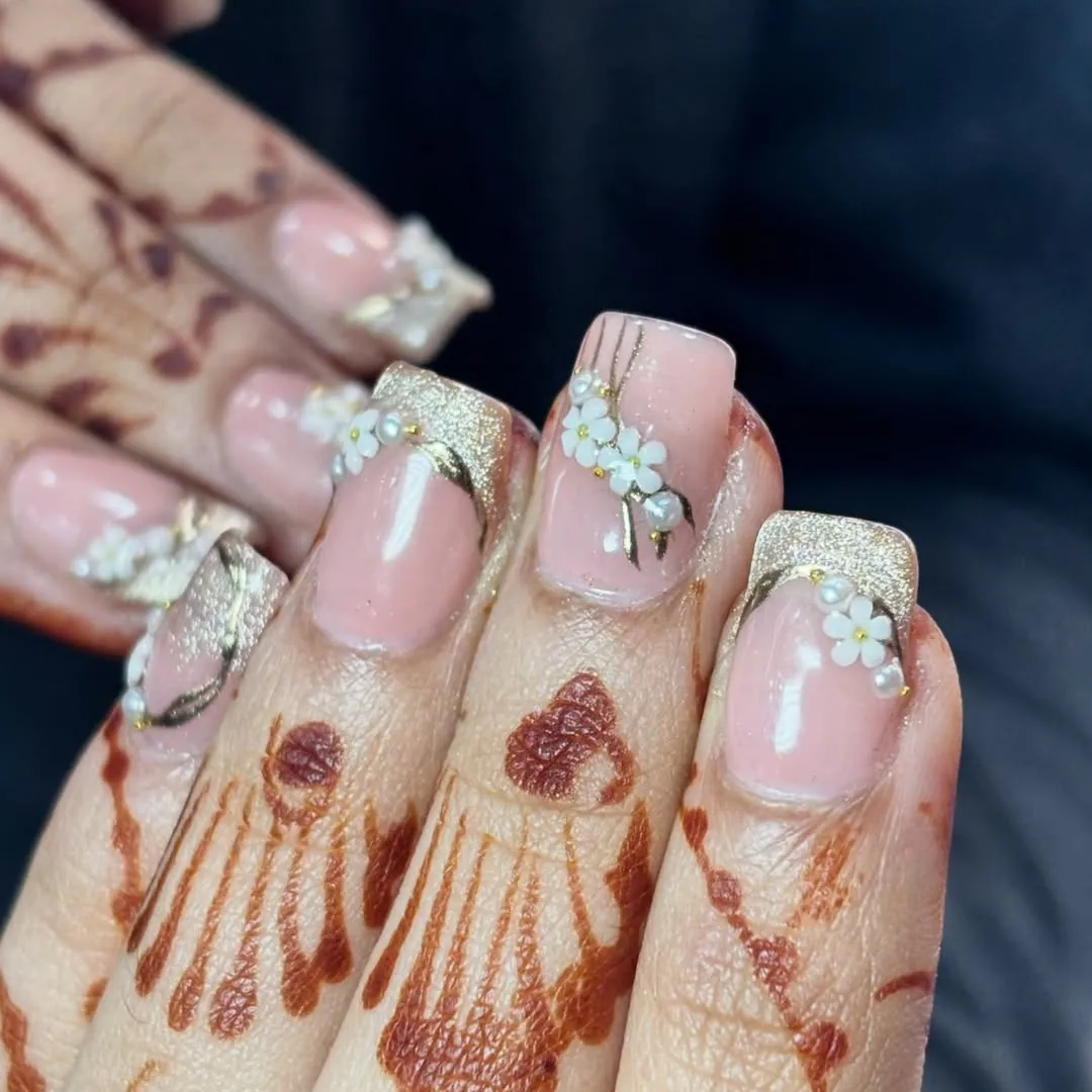 Pink nails with gold glitter tips and small white floral clusters