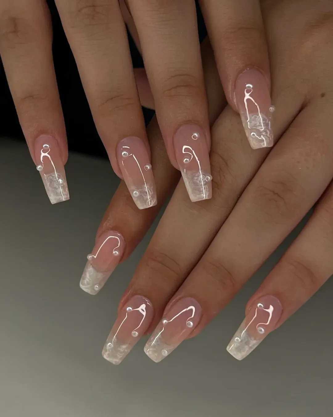 Long square pink nails with milky marbling, white swirls, and pearl accents