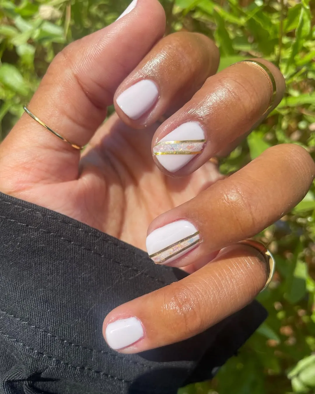 Glossy white nails with diagonal gold and iridescent stripe accents