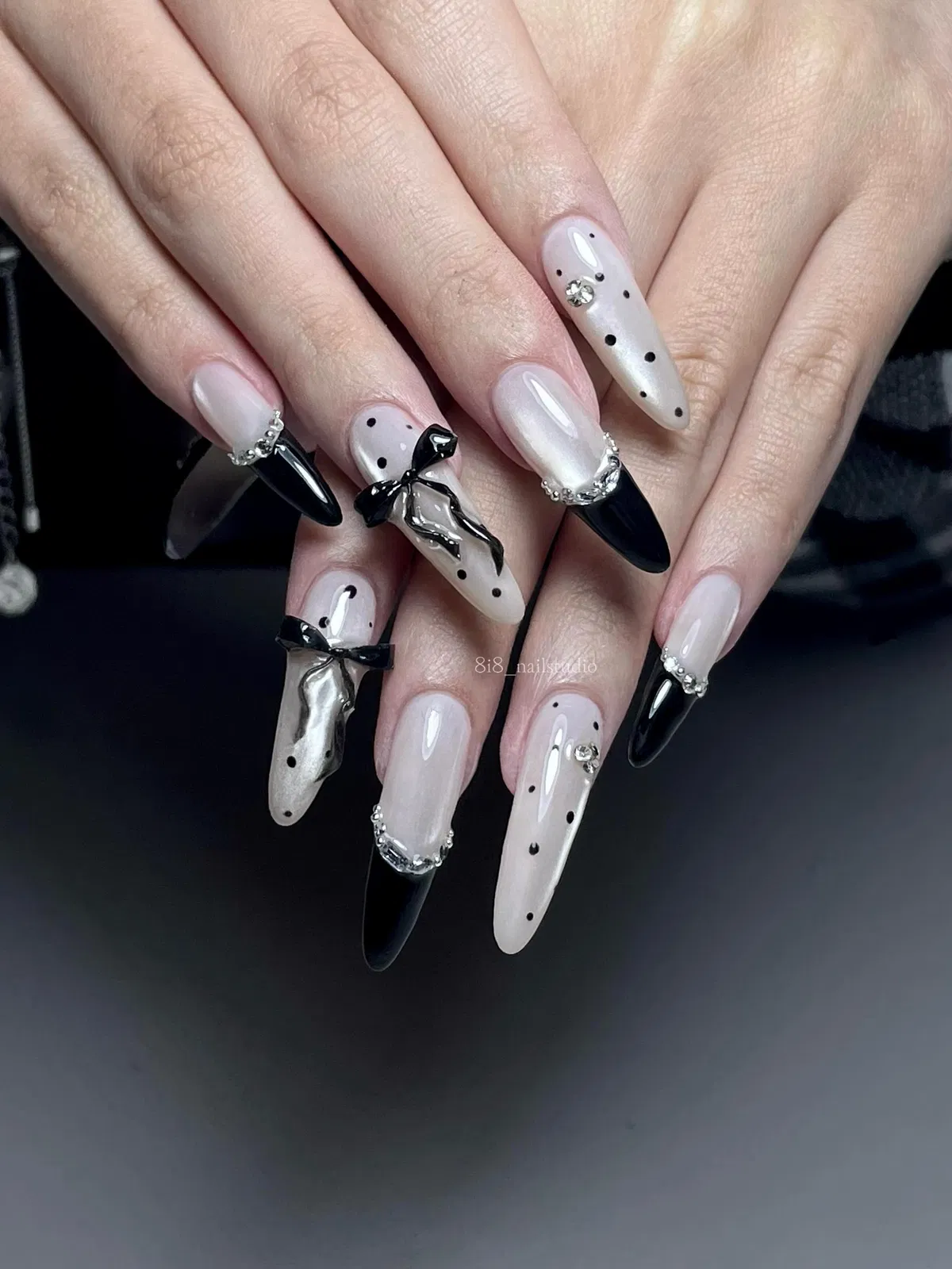 Stiletto nails with polka dot tips, curved sparkle borders, and a bow accent