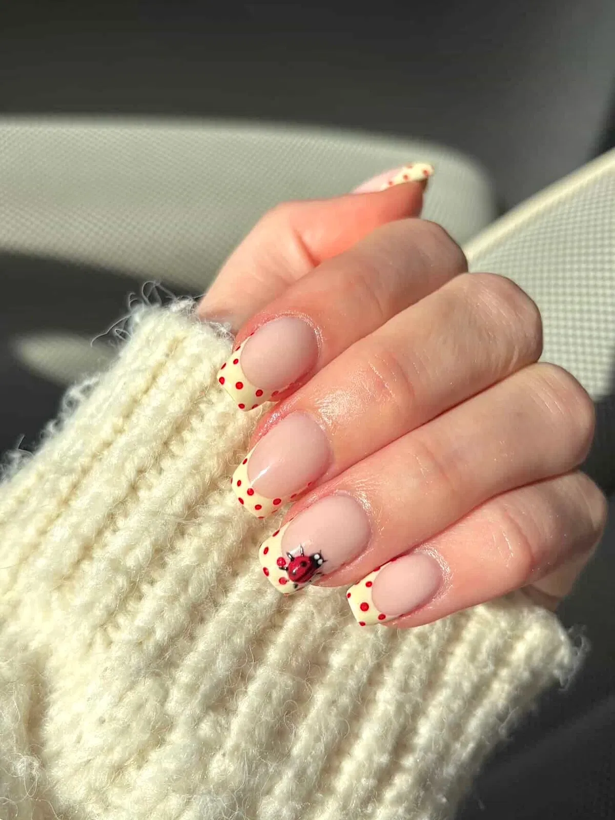 Square nude nails with red polka-dot yellow tips and ladybug accent