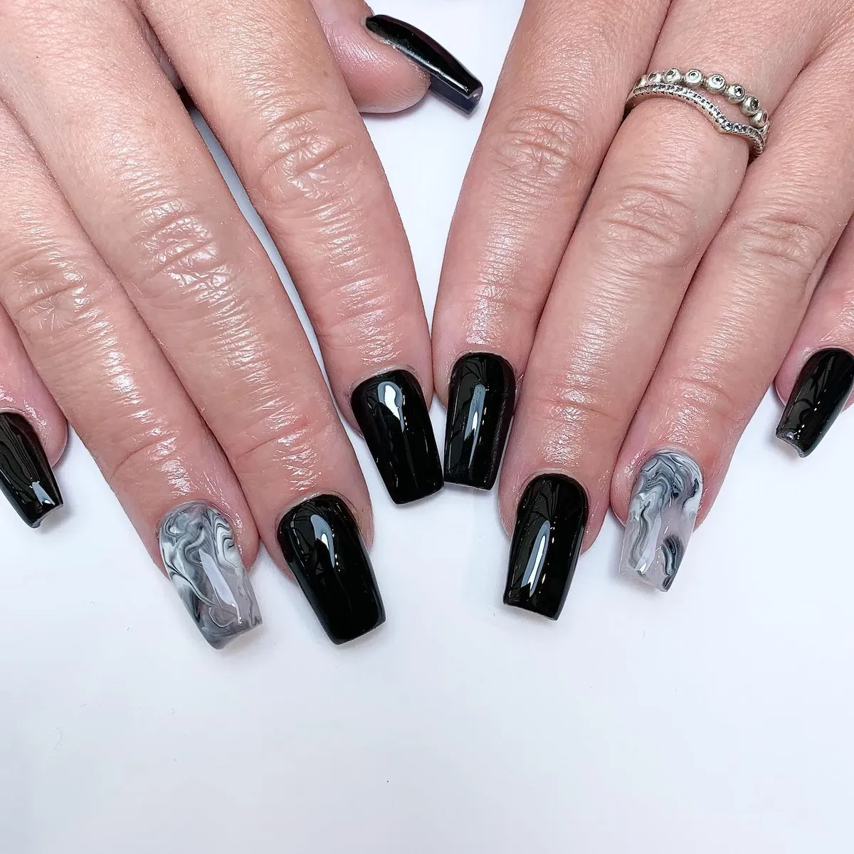 Glossy black nails with white swirl lines and small rhinestone accents