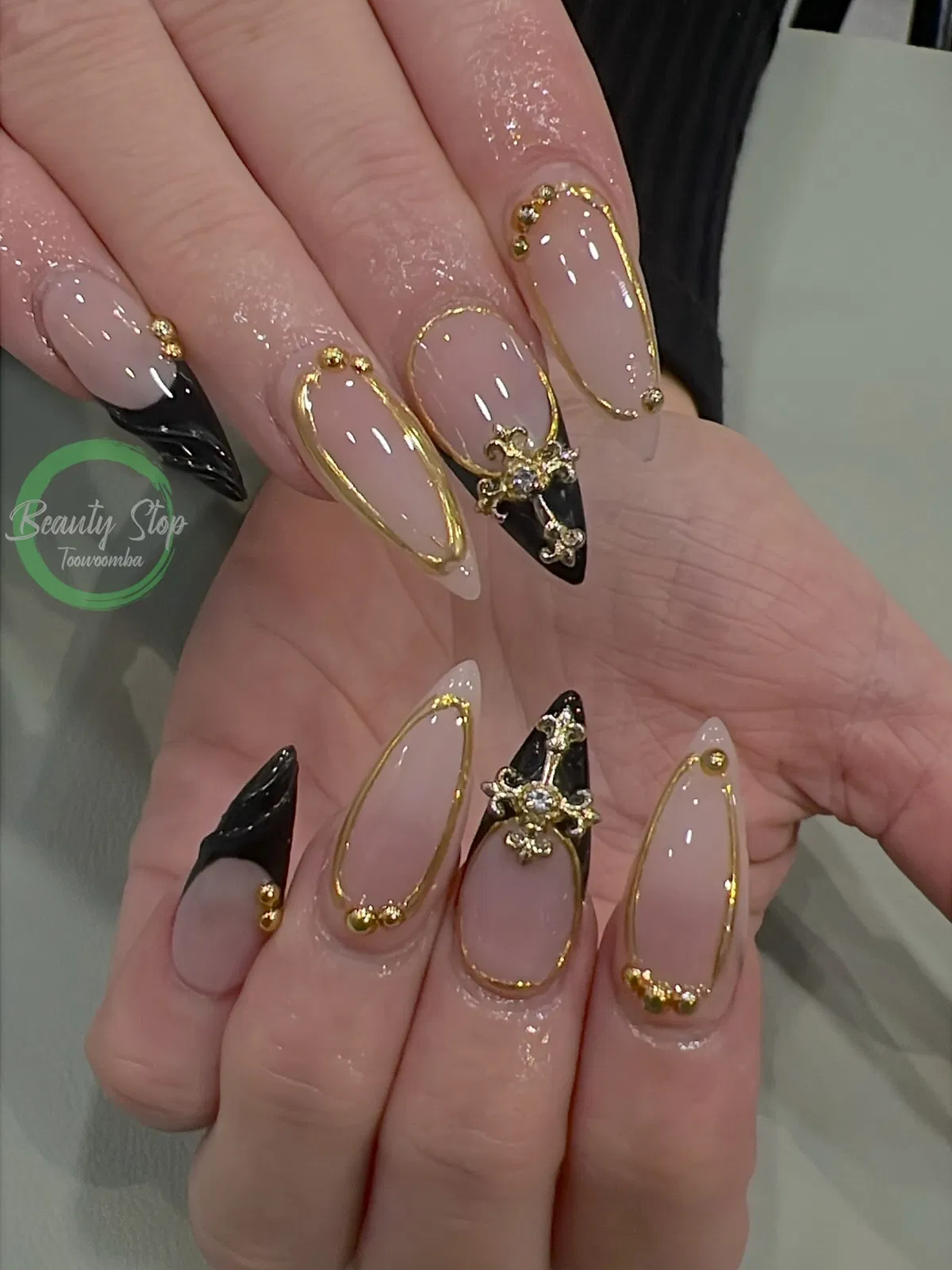 Gold-framed nude nails with black tips and rhinestone-like centerpiece charm