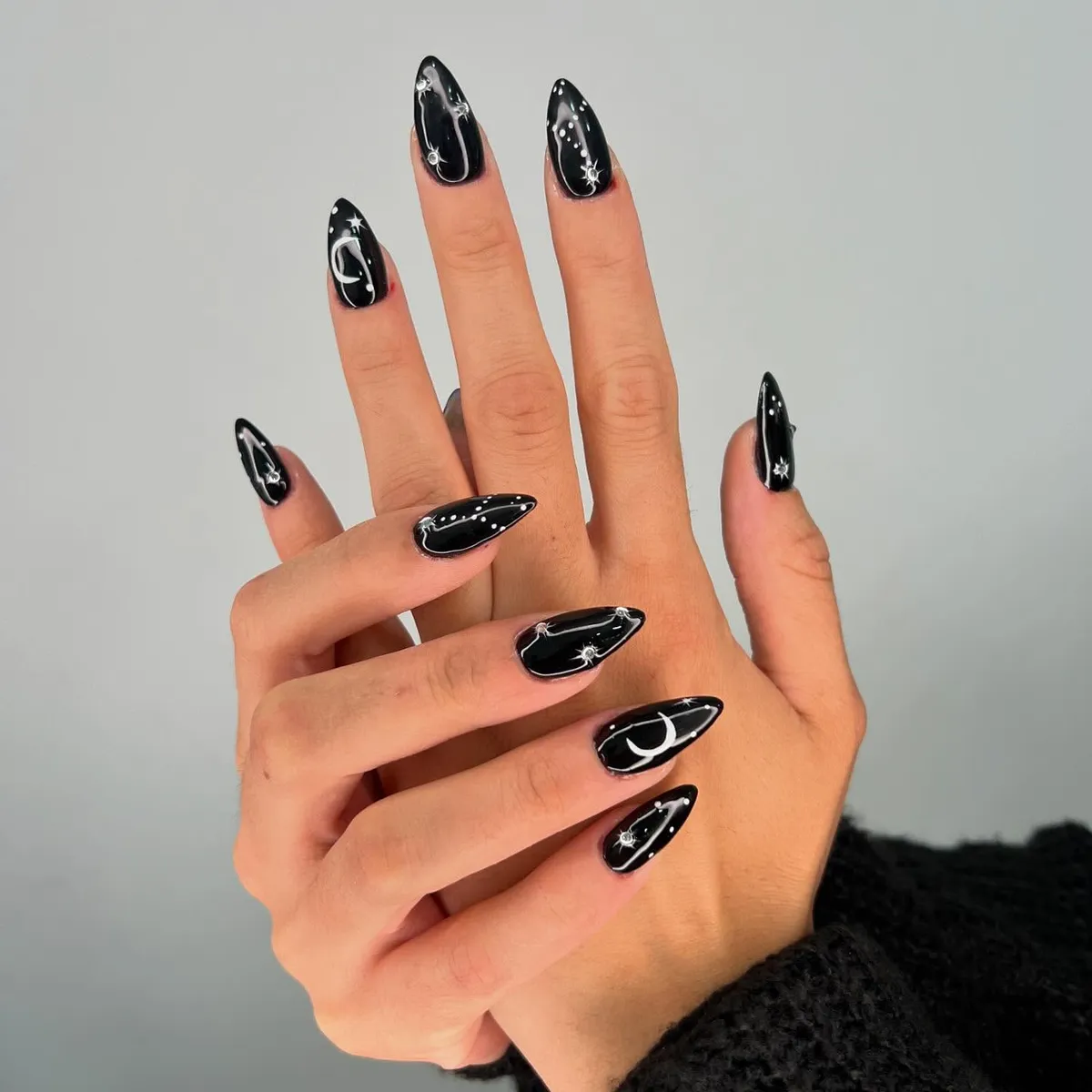 Black stiletto nails with white crescent moons, dotted trails, and star-like accents