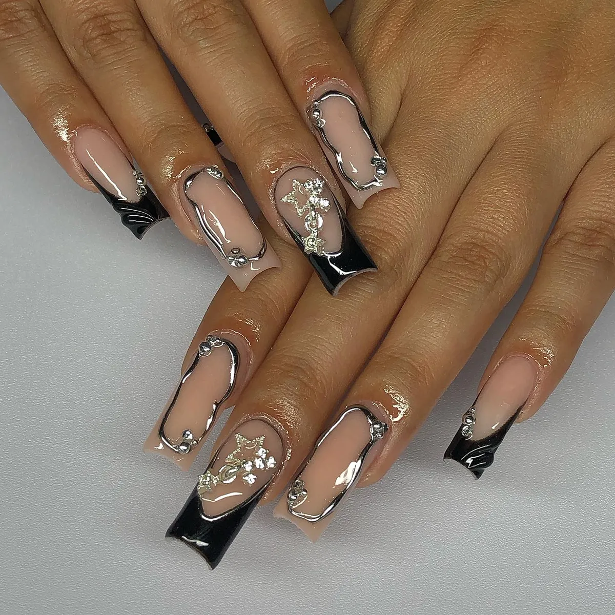 Nude-and-black square nails with silver outlines and raised metallic decorations
