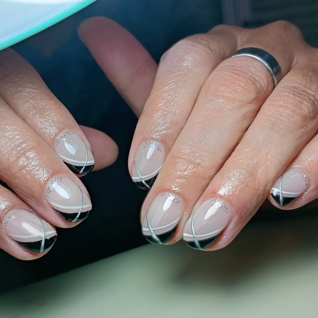 Taupe nails with black tips, white crossing lines, and subtle glitter accents