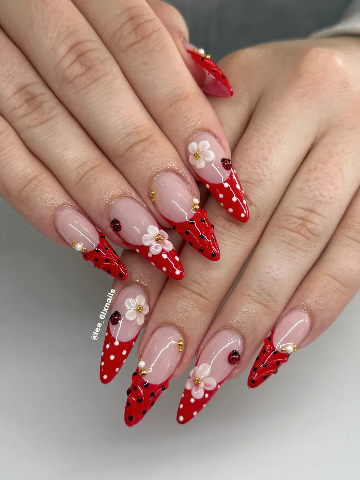 Red-tipped nails with 3D white flowers, polka dots, and ladybug details