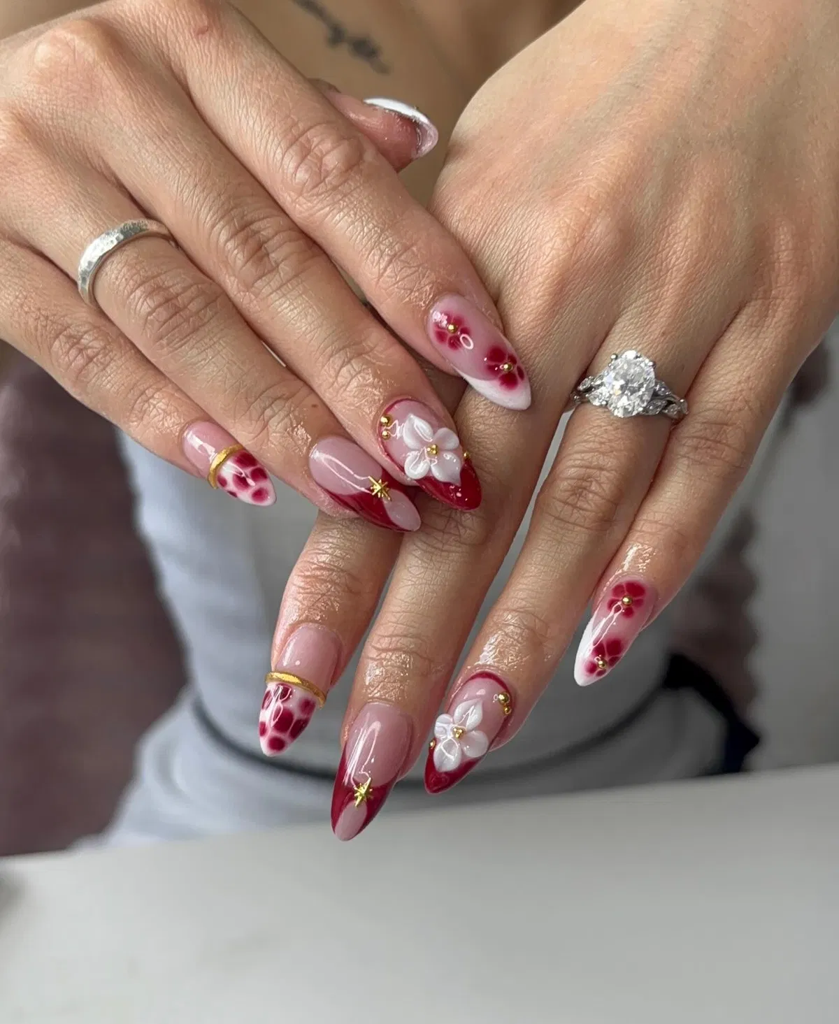 Red-tipped nude nails with 3D white flowers and gold accents