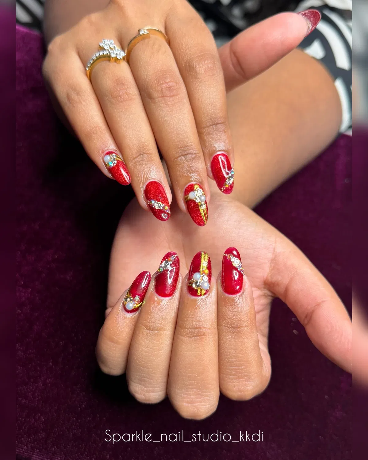 Bright red glossy nails with gold striping and clustered embellishments